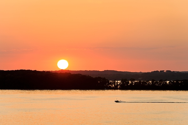 With a fiery sunset lighting the way, a motorboat crosses Lake Mendota.