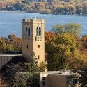 A stone tower is shown with a lake and trees in the background.