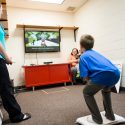 Xavier Hansen stands on a Wii Connect balance board and practices a Wii ski jump pose while mirroring his body position to match that of a video-game shape displayed on a computer monitor.