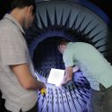 Photo: Amin Momeni illuminates the antenna-testing chamber while Nader Behdad installs a phased-array antenna. The flat surface consists of multiple precisely-positioned elements that convert spherical radio signals into single-column beams.