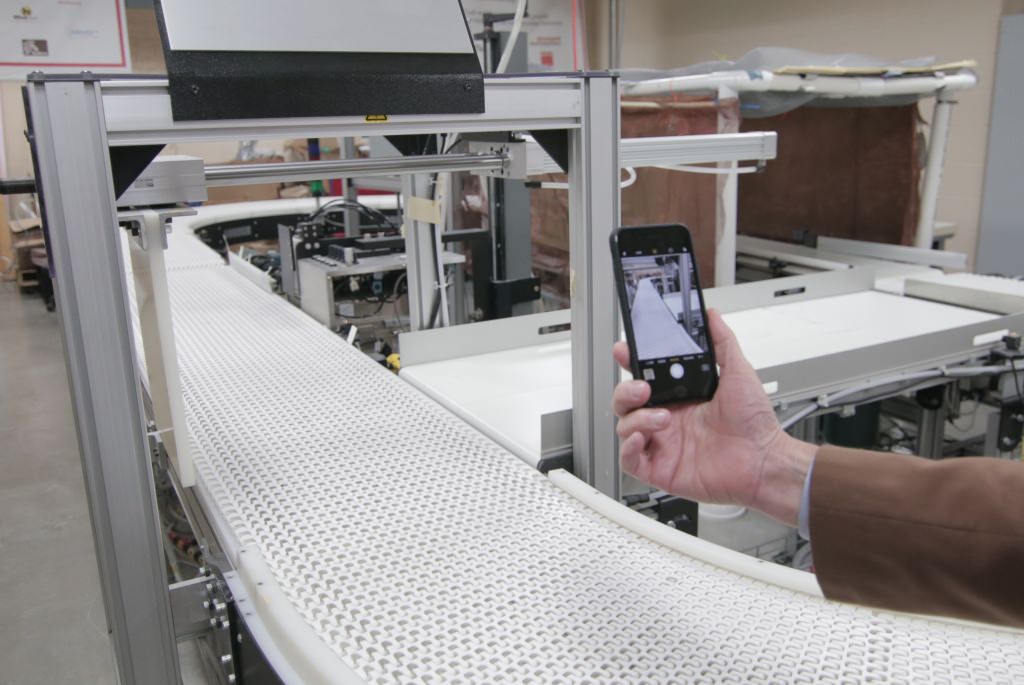 Photo: Man holding cellphone up to conveyor belt