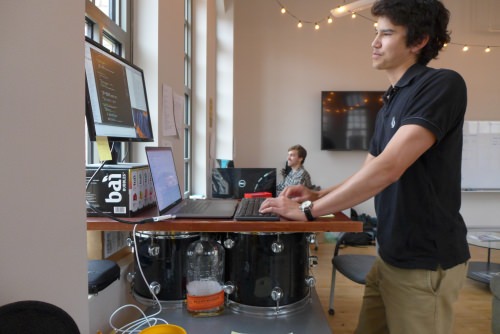 Nick Glattard works on a desk resting on drums; home-made music provides stress relief amid long sessions of writing computer code. 