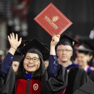 A graduate holds up her diploma cover to show family during UW-Madison's spring commencement ceremony at the Kohl Center at the University of Wisconsin-Madison on May 12, 2017. The indoor graduation was attended by approximately 830 doctoral, MFA and medical student degree candidates, plus their guests. (Photo by Bryce Richter / UW-Madison)