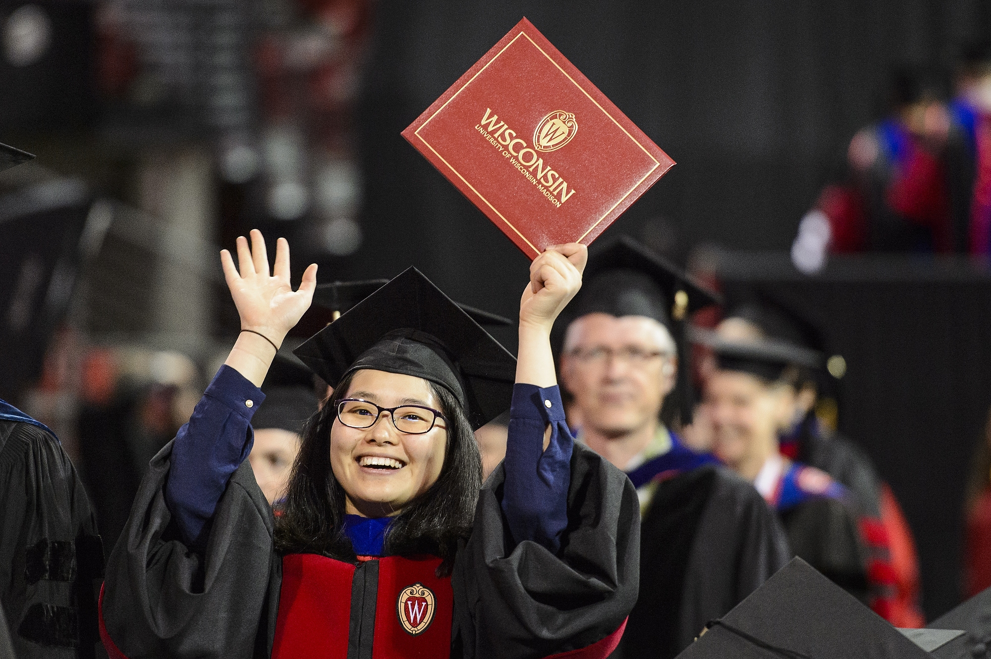 A graduate holds up her diploma cover to show family during UW–Madison's spring commencement ceremony at the Kohl Center at the University of Wisconsin–Madison on May 12, 2017. The indoor graduation was attended by approximately 830 doctoral, MFA and medical student degree candidates, plus their guests. (Photo by Bryce Richter / UW–Madison)