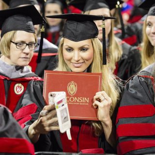 A graduate takes a selfie with her diploma cover during UW-Madison's spring commencement ceremony at the Kohl Center at the University of Wisconsin-Madison on May 12, 2017. The indoor graduation was attended by approximately 830 doctoral, MFA and medical student degree candidates, plus their guests. (Photo by Bryce Richter / UW-Madison)