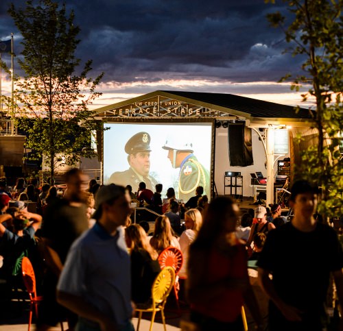 People relax in a recently-renovated section of seating at the Memorial Union Terrace along Lake Mendota at the University of Wisconsin–Madison and watch the 1978 movie "National Lampoon's Animal House" as dusk falls to a summer night on June 27, 2016. Shown on the Terrace's new performance stage, the film screening is part of the Lakeside Cinema programming led by the Wisconsin Union Directorate (WUD). (Photo by Jeff Miller/UW-Madison)