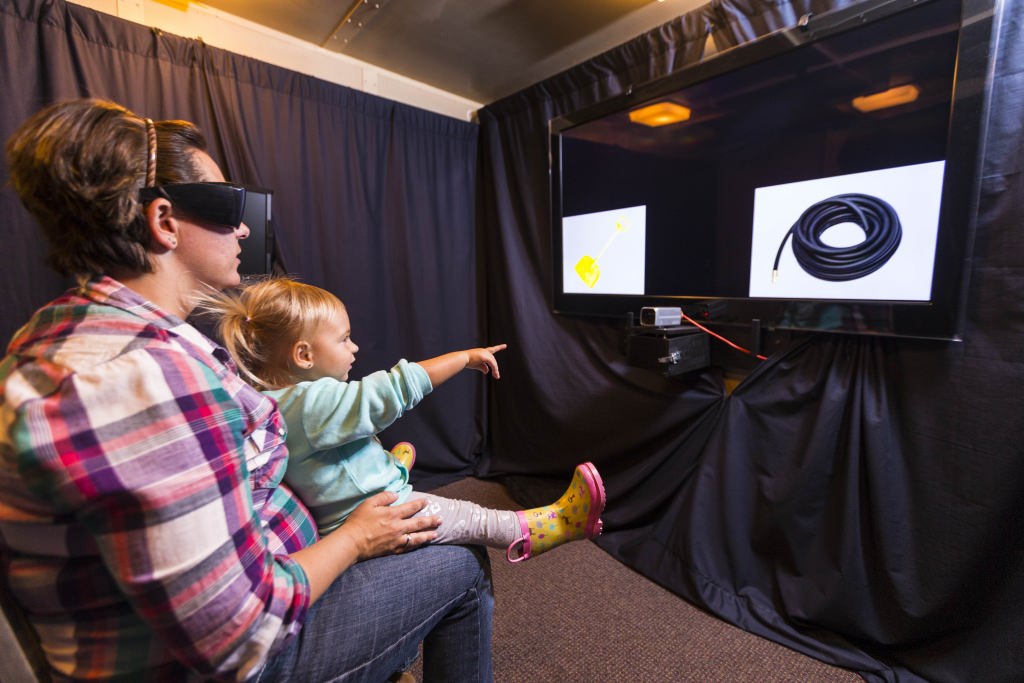 Photo: Infant on an adult's lap pointing to video screen