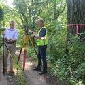 At a location in La Crosse County, state cartographer Howard Veregin, on left, stands next to a modern, GPS-assisted surveying instrument. On right, Bryan Meyers, La Crosse County Surveyor and president of the Wisconsin County Surveyors Association, stands with a transit like the one likely used to survey this site. 
