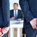 Photo: Two people in suits holding gift-wrapped boxes behind their backs, facing a man at a desk