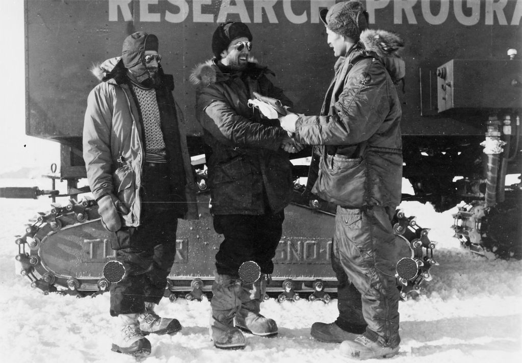 Photo: Charles Bentley shaking hands with unidentified man in front of Antarctic research vehicle