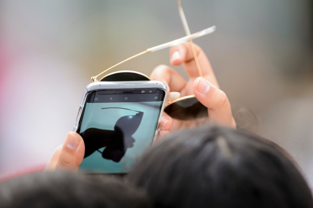 An observer uses sunglasses held in front of a smartphone to look at the moon as it passes orbit in front of the sun for a maximum 85-percent solar eclipse -- as seen at the Memorial Union Terrace at the University of Wisconsin-Madison -- on Aug. 21, 2017. A total-solar eclipse was visible, for the first time in almost 100 years, along a coast-to-coast path across the middle of the United States from Oregon to the Carolinas. (Photo by Jeff Miller / UW-Madison)