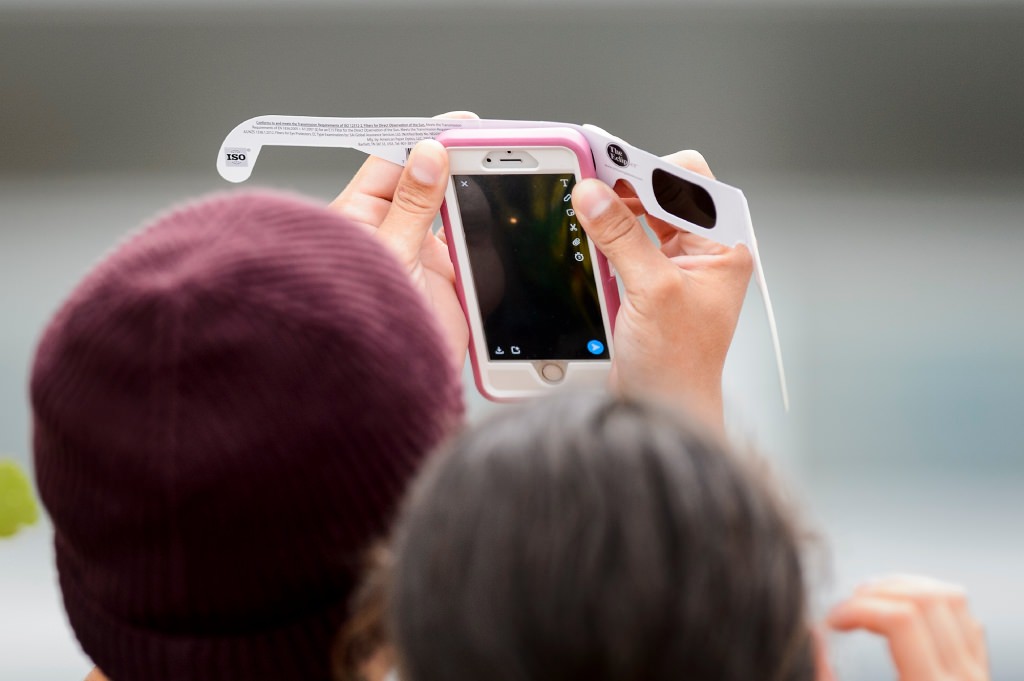 An observer uses sunglasses held in front of a smartphone to look at the moon as it passes orbit in front of the sun for a maximum 85-percent solar eclipse -- as seen at the Memorial Union Terrace at the University of Wisconsin-Madison -- on Aug. 21, 2017. A total-solar eclipse was visible, for the first time in almost 100 years, along a coast-to-coast path across the middle of the United States from Oregon to the Carolinas. (Photo by Jeff Miller / UW-Madison)