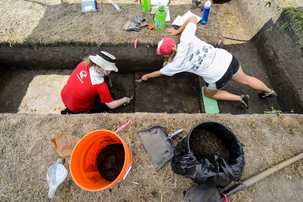 Photo: People digging with trowels in archaeological site