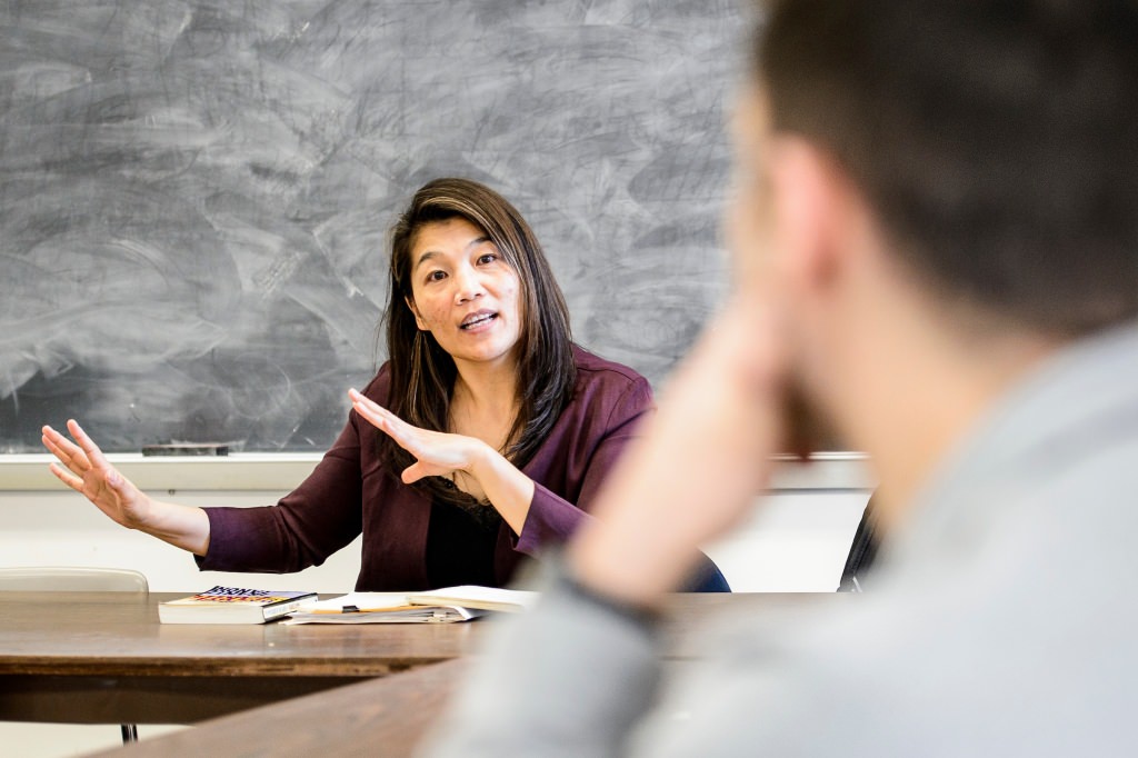 Photo: Cindy I-Fen Cheng sitting in front of chalk board talking to student