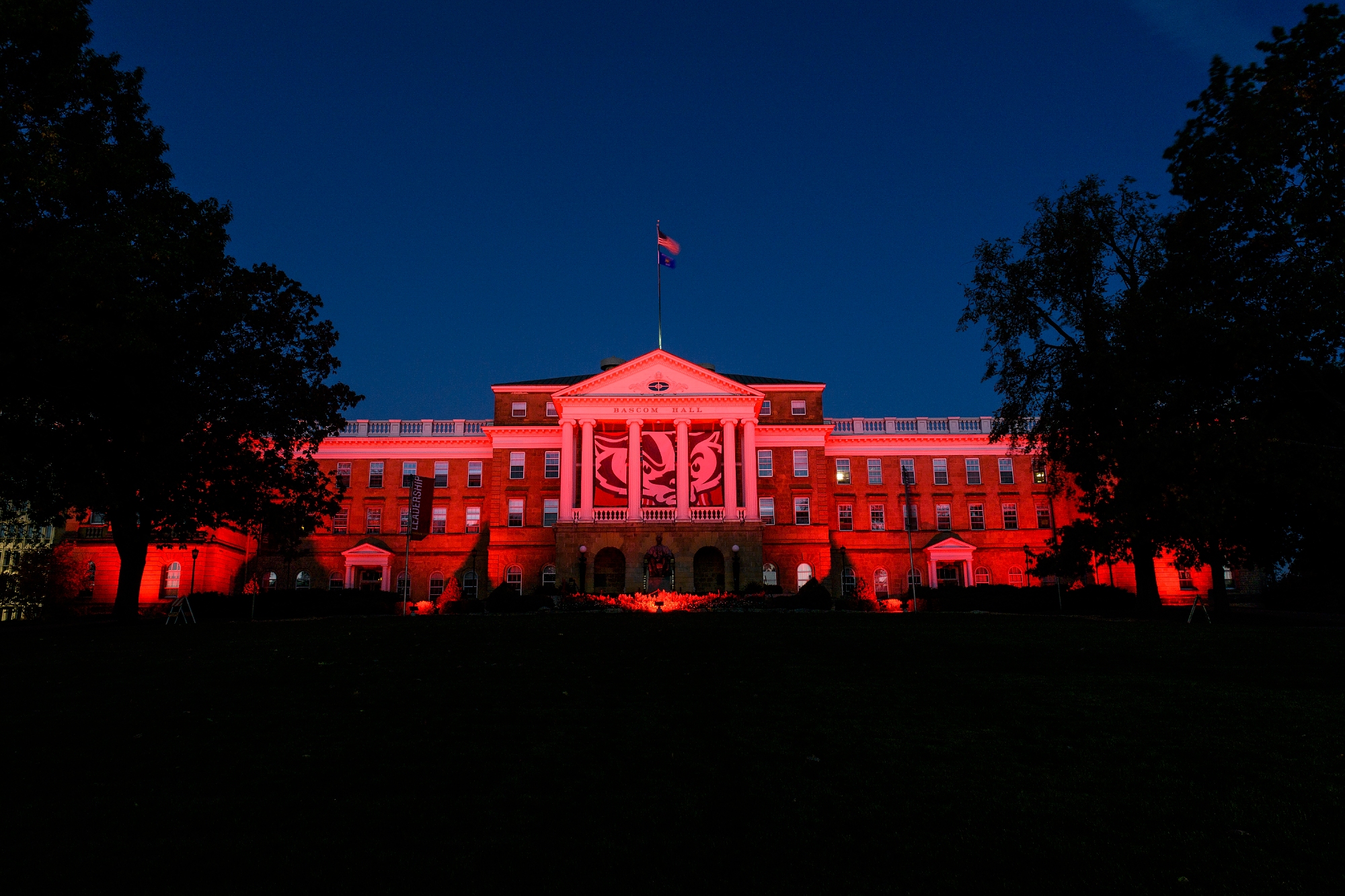 n honor of UW–Madison's Homecoming Week, red-colored accent lighting illuminates the exterior of Bascom Hall and terrace plantings surrounding the Abraham Lincoln statue at the University of Wisconsin–Madison as dawn brightens the night sky on Oct. 20, 2017. Hanging between the building's column is a graphic banner of UW–Madison mascot Bucky Badger. (Photo by Jeff Miller / UW–Madison)