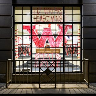 Hand-painted in red, the letter W and a homecoming message displayed on the main entrance window at Elizabeth Waters Residence Hall at the University of Wisconsin-Madison reflects some school spirit during an autumn night on Oct. 18, 2017. (Photo by Jeff Miller / UW-Madison)