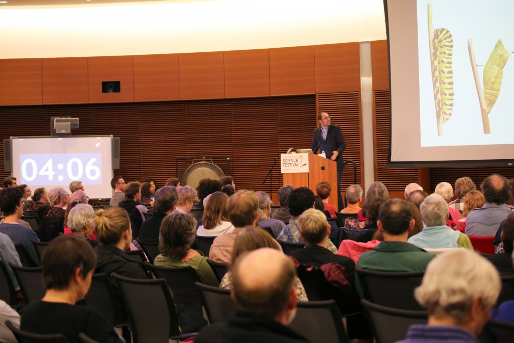 Photo: Josh Coon speaking to auditorium crowd