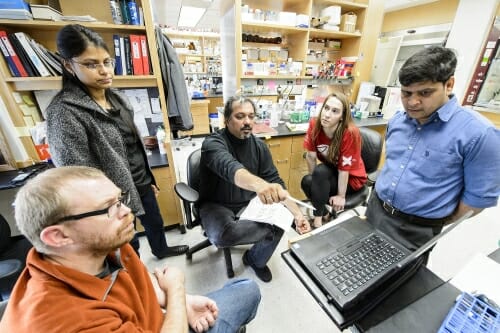 Photo: Aseem Ansari gesturing toward computer and talking with his research team