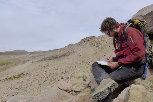 Photo: Nathan Andersen sitting at volcano site taking notes