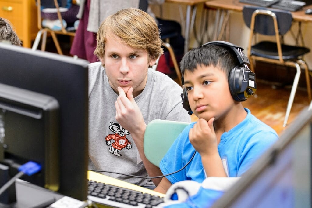 Photo: College student and elementary student looking at computer screen with similar poses of hands on their chins