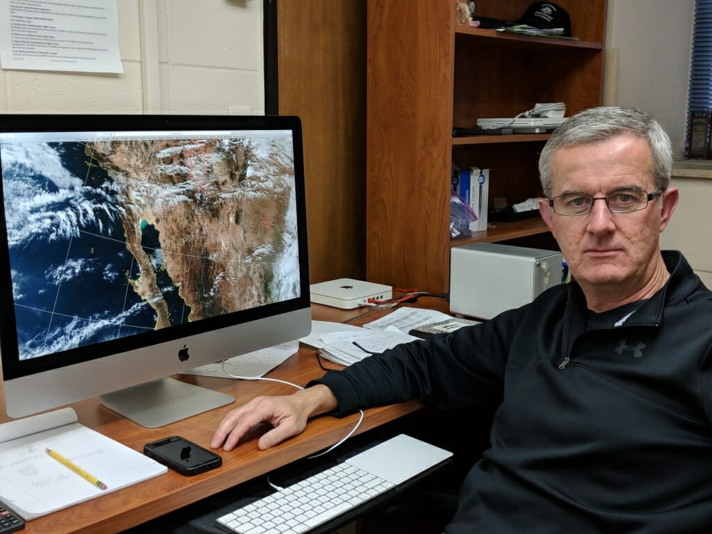 Photo: Liam Gumley sitting in front of computer screen displaying satellite image