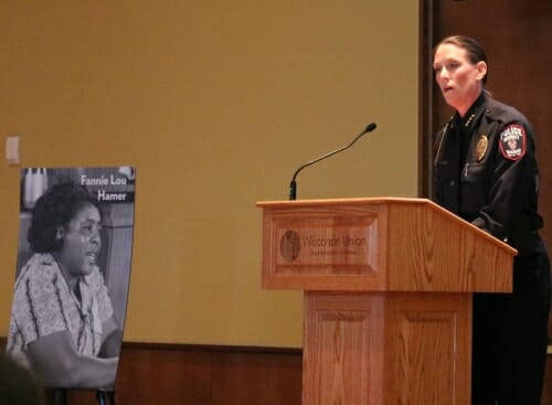 Photo: Kristen Roman speaking at podium with Fanny Lou Hamer poster next to her