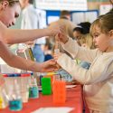 Photo: Student handing test tube to young girl