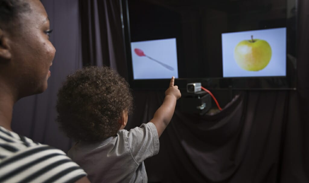 Photo: Woman holding infant pointing at screens