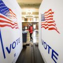 View of a person standing in the distance from between 2 voting booths with American flags and the word 