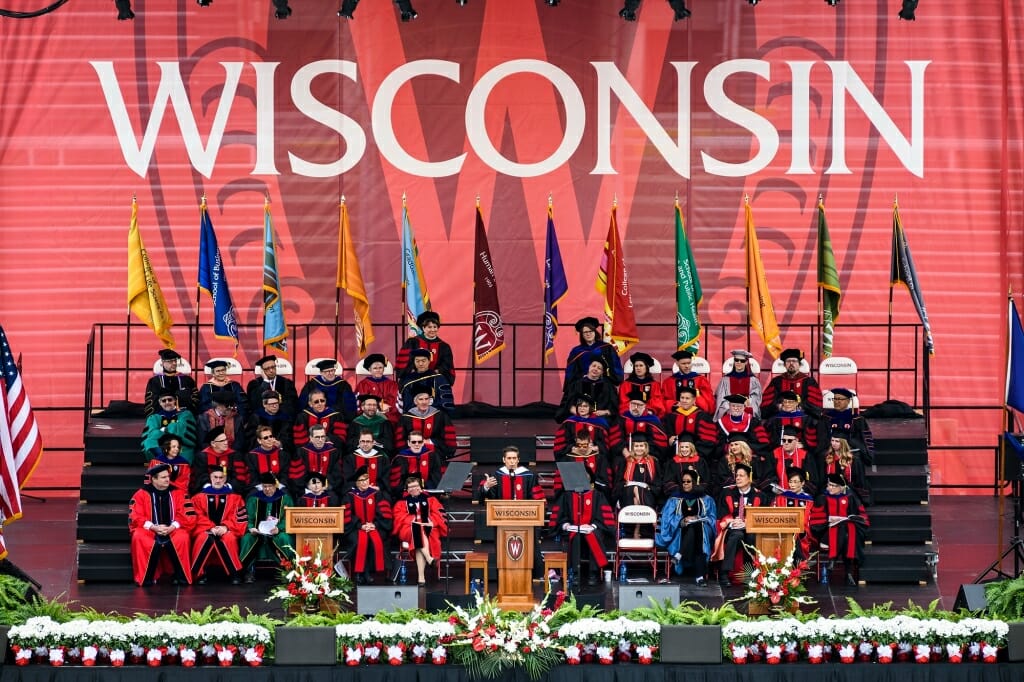 Photo of speaker David Muir flanked by the platform party of university leaders and senior class officers.