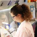 Photo: Student in lab coat reaching into enclosure