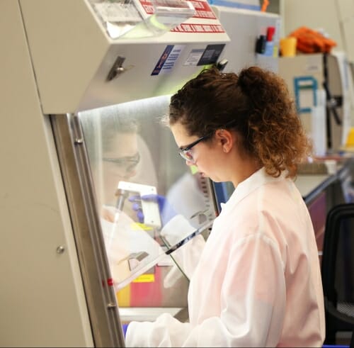 Photo: Hailey in lab coat reaching into lab enclosure