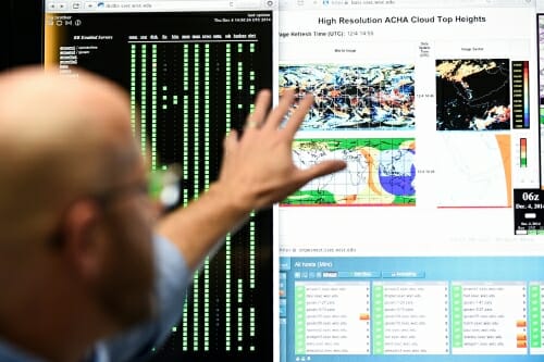 Photo: Researcher gesturing toward monitors showing colorful graphs