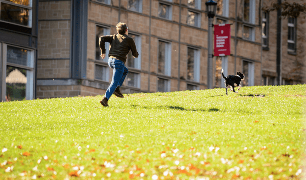 A photo of a student jogging up Bascom Hill with his dog. 