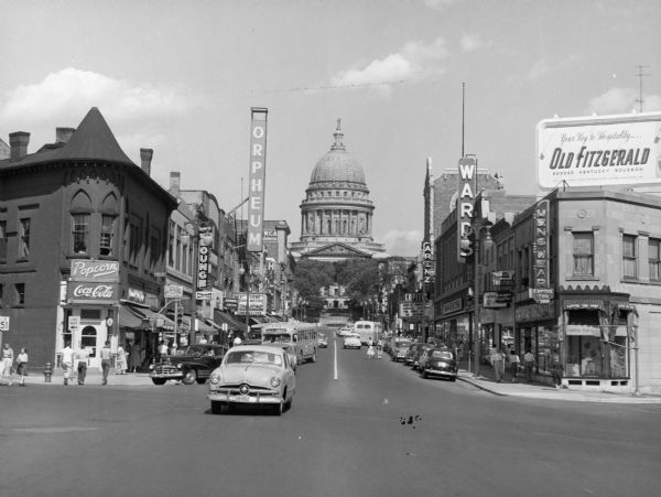 View up State Street towards the Wisconsin State Capitol taken from the West Johnson Street intersection. Businesses include the Orpheum Theater, Arenz, and Ward's. There is a billboard for Old Fitzgerald Kentucky bourbon on the roof on the right.