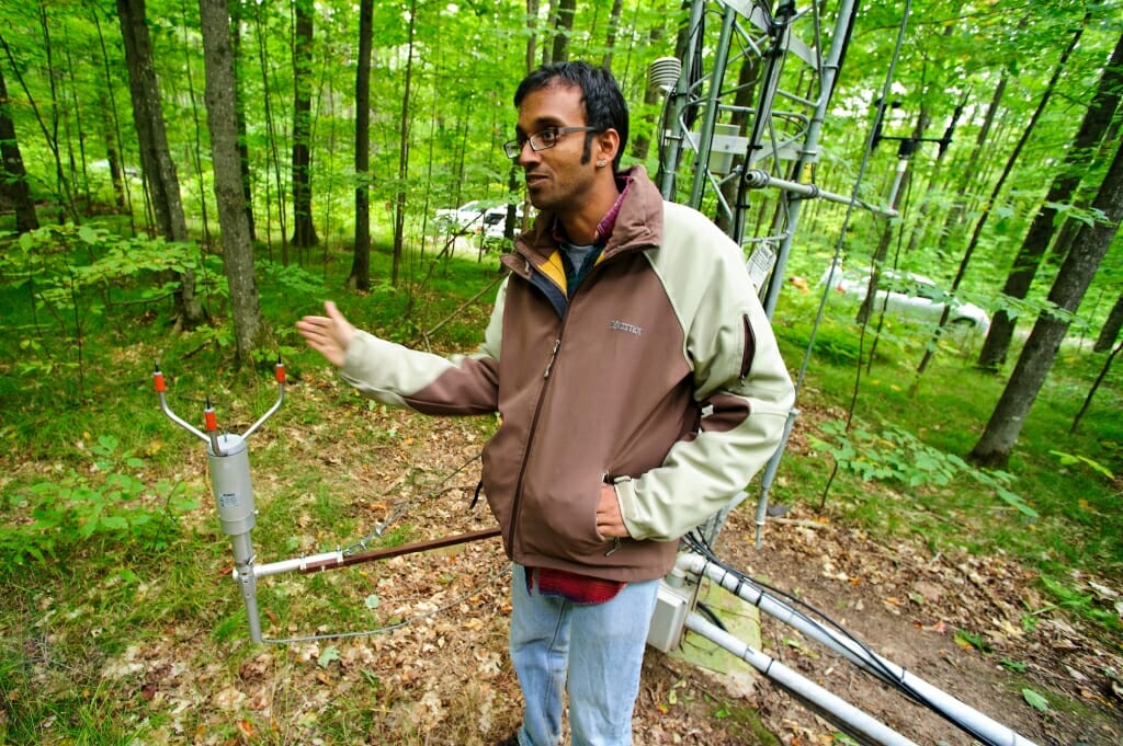 Photo: Desai gesturing by base of tower in forest