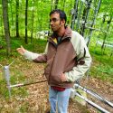 Photo: Desai gesturing by base of tower in forest