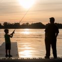 Photo: A boy casts a line into a lake as a man watches.