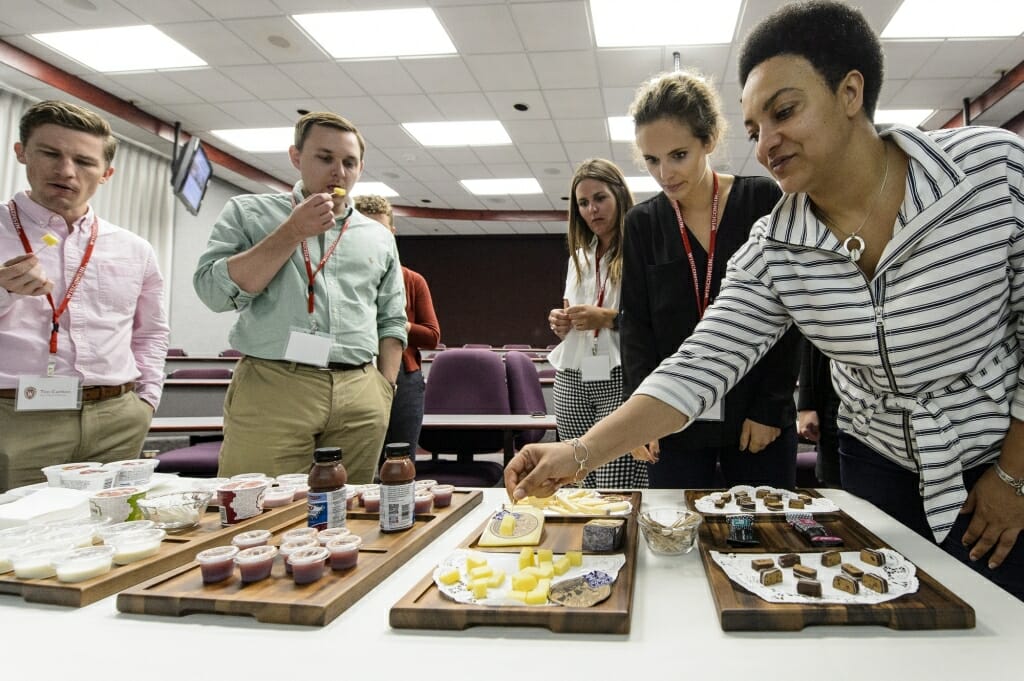 Photo: Group of people standing around table eating small cubes of cheese on toothpicks