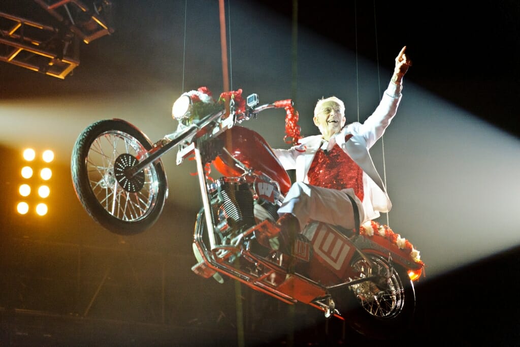 Photo: Leckrone suspended on motorcyle, waving to audience