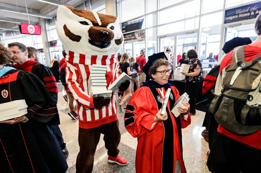 Photo: Bucky Badger standing behind Rebecca Blank holding a stack of books