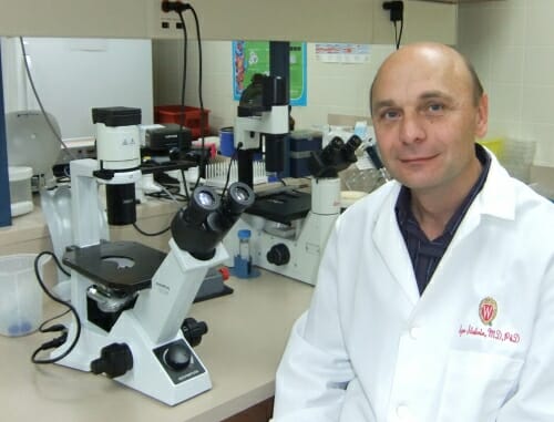 Photo: Igor Slukvin in white lab coat sitting next to mircroscope