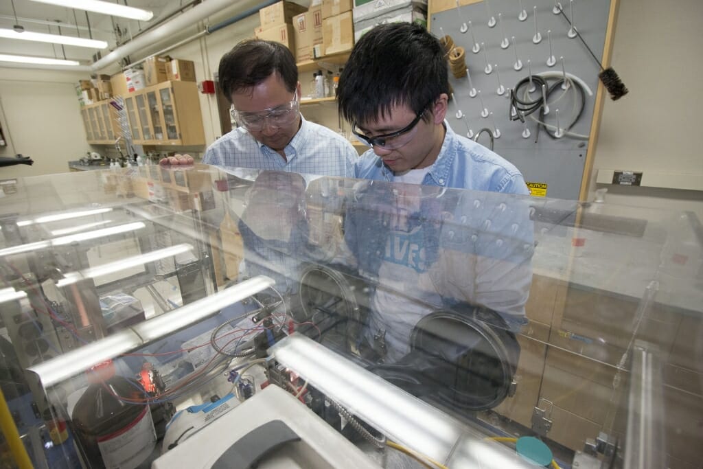 Photo of Song Jin, left, and graduate student Wenjie Li observing their lab-scale device for storing and releasing solar energy. 