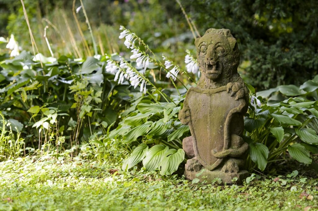 Photo: Stone gargoyle sitting in garden in front of hostas