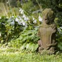 Photo: Stone gargoyle sitting in garden in front of hostas