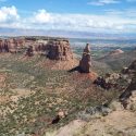 Colorado National Monument AltText: towers and mesas of brown rock in the midground with shrubby desert ground taking up most of the foreground