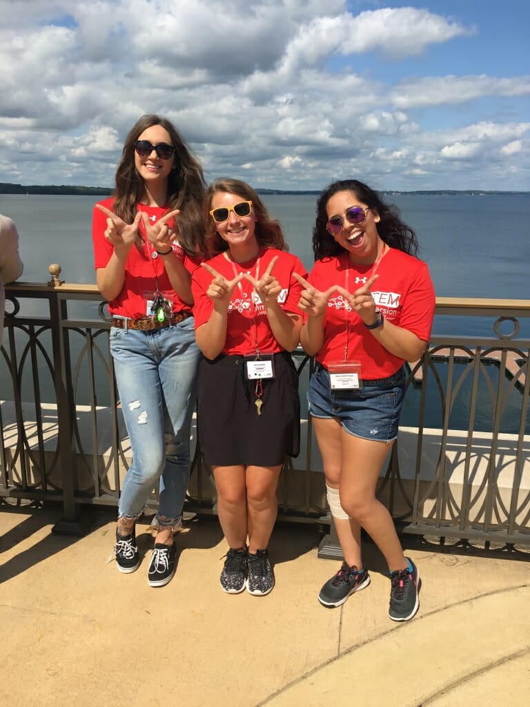 A photo of three college students holding their hands in the shape of a "W" for Wisconsin. 