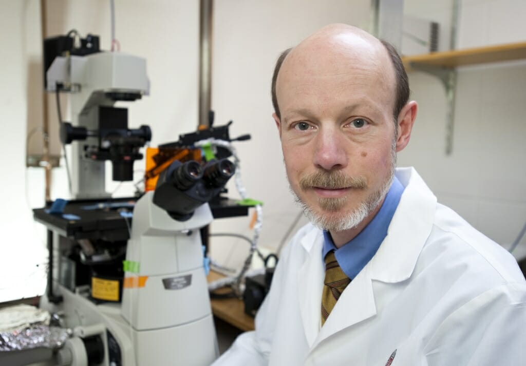 Photo of Tim Kamp wearing a white coat by a microscope.