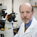 Photo of Tim Kamp wearing a white coat by a microscope.