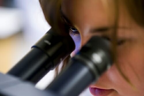 Woman peers into microscope.